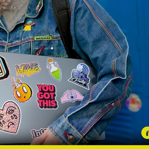 Menina no colégio carregando notebook cheios de adesivos na mão